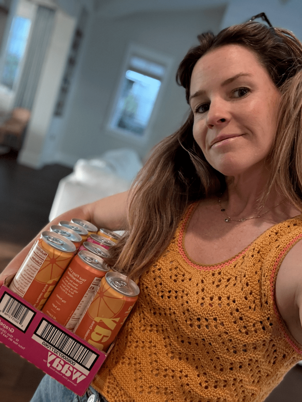 Morgan holding a pack of Waay protein drinks in a room with neutral decor.